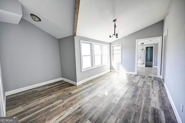 empty room featuring baseboards, wood finished floors, and vaulted ceiling