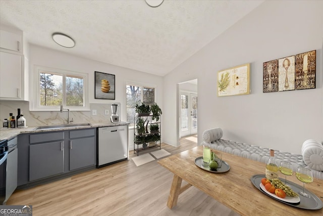 kitchen featuring dishwasher, light wood-style flooring, vaulted ceiling, gray cabinets, and a sink