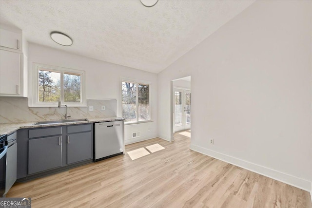 kitchen with visible vents, light wood-style flooring, vaulted ceiling, a sink, and dishwasher