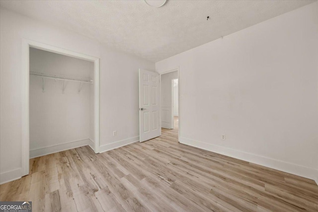 unfurnished bedroom with a textured ceiling, a closet, baseboards, and wood finished floors