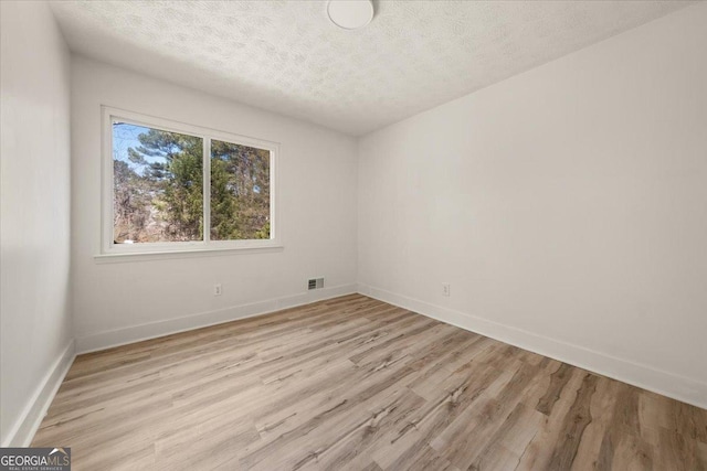 empty room featuring visible vents, baseboards, light wood-style flooring, and a textured ceiling