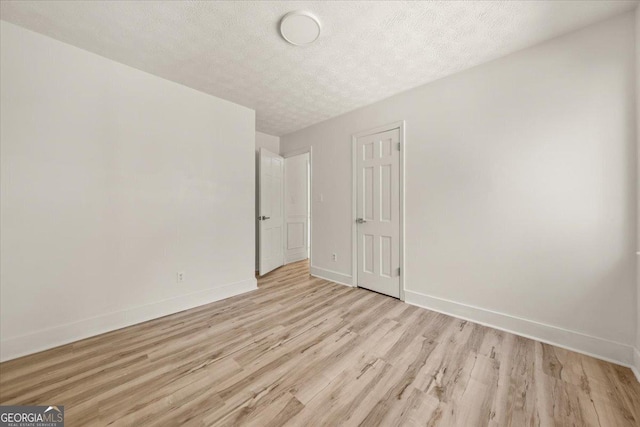 spare room featuring baseboards, a textured ceiling, and light wood-style floors