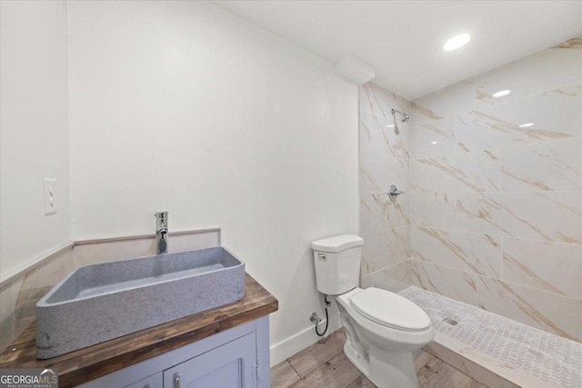 full bathroom featuring toilet, wood finished floors, vanity, baseboards, and tiled shower