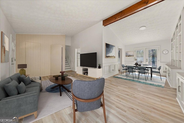 living area with vaulted ceiling with beams, a decorative wall, light wood-style flooring, a textured ceiling, and stairs