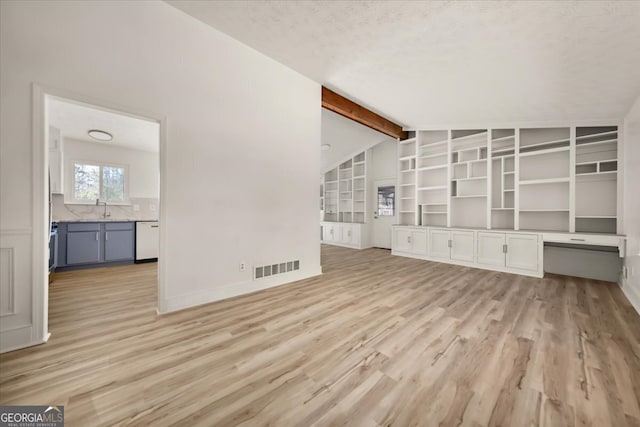 unfurnished living room featuring lofted ceiling with beams, light wood-style flooring, a sink, visible vents, and built in desk