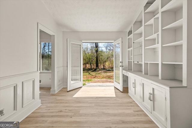 doorway with wainscoting, a decorative wall, light wood-style flooring, and a textured ceiling