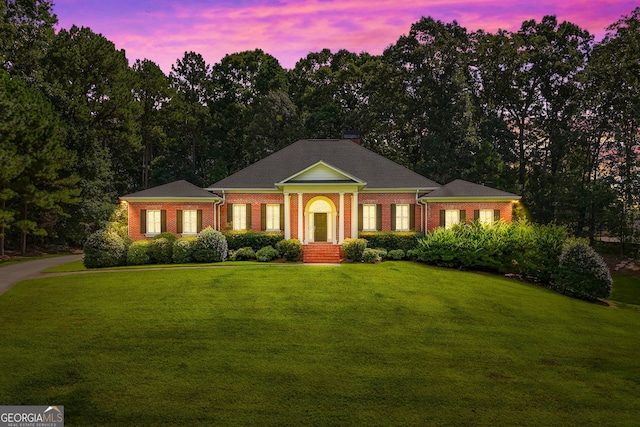 neoclassical home featuring a chimney, a lawn, and brick siding