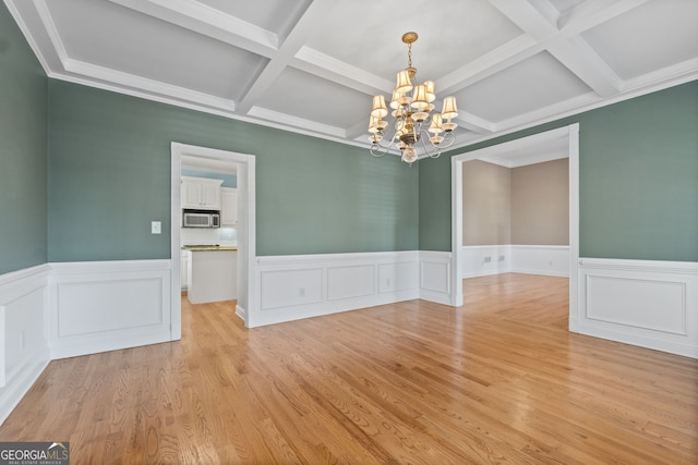 unfurnished dining area featuring beam ceiling, a wainscoted wall, a notable chandelier, and light wood finished floors