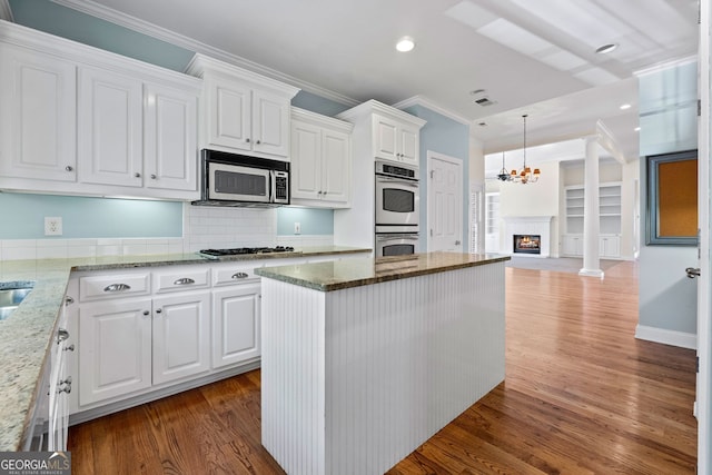 kitchen with stone counters, wood finished floors, white cabinetry, ornamental molding, and appliances with stainless steel finishes