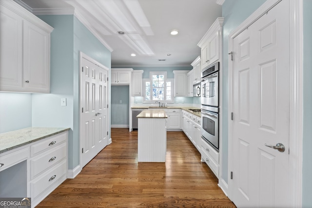 kitchen with dark wood-style floors, a kitchen island, appliances with stainless steel finishes, ornamental molding, and white cabinetry