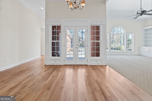 doorway to outside featuring baseboards, a towering ceiling, wood finished floors, crown molding, and french doors