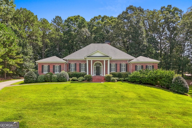 neoclassical home with a chimney, a front lawn, and brick siding