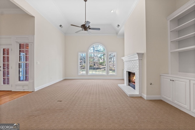 unfurnished living room with ornamental molding, a brick fireplace, light colored carpet, and a ceiling fan