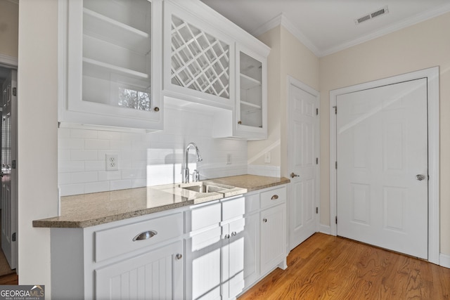 kitchen featuring light stone counters, ornamental molding, glass insert cabinets, light wood-type flooring, and a sink