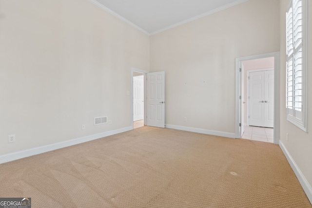 empty room featuring crown molding, visible vents, a high ceiling, light carpet, and baseboards