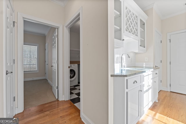 kitchen with washer / dryer, white cabinets, glass insert cabinets, crown molding, and a sink