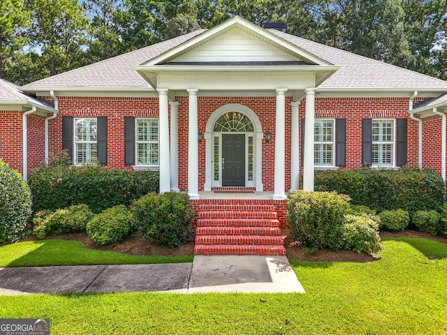 view of front of property featuring covered porch, a shingled roof, a front lawn, and brick siding