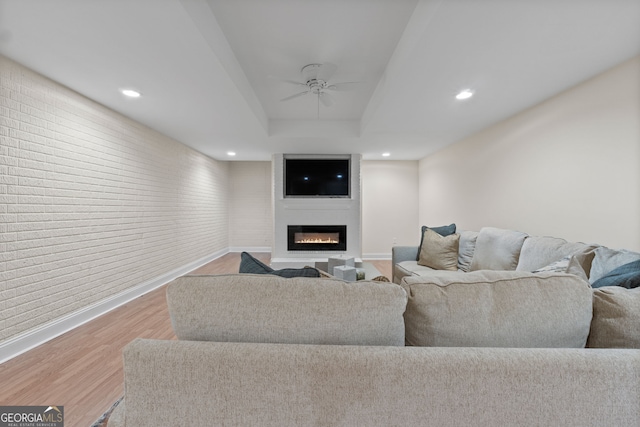 living room with a large fireplace, ceiling fan, baseboards, and wood finished floors