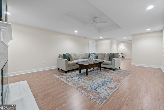 living area with a brick fireplace, baseboards, a raised ceiling, and light wood-style floors