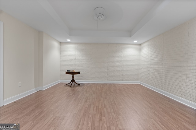 empty room featuring a tray ceiling, baseboards, brick wall, and wood finished floors