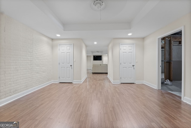 interior space with light wood finished floors, recessed lighting, a raised ceiling, brick wall, and baseboards