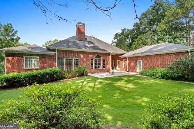 rear view of property with brick siding, a patio, a chimney, and a lawn