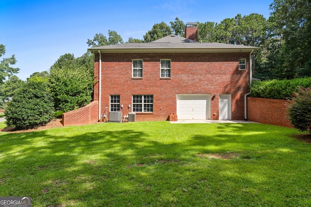 back of house with an attached garage, brick siding, a yard, driveway, and a chimney