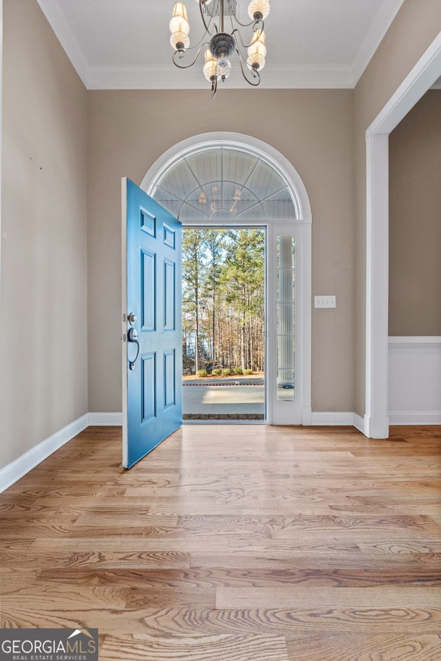 foyer entrance with baseboards, a chandelier, wood finished floors, and ornamental molding