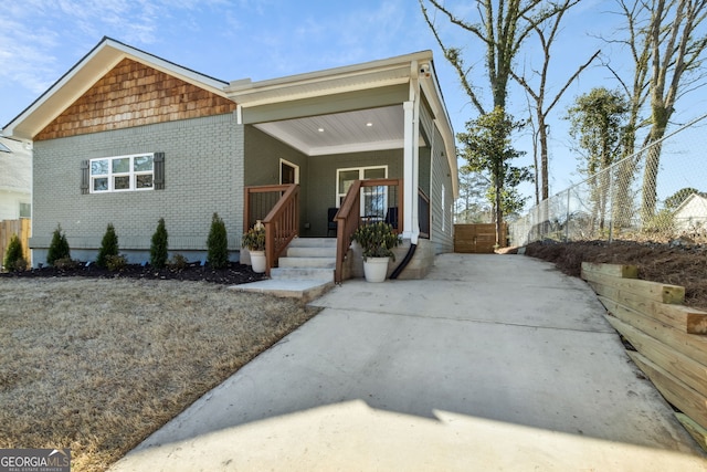 view of front of house with covered porch, fence, and brick siding