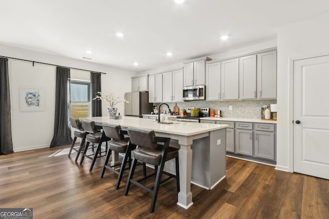 kitchen featuring tasteful backsplash, an island with sink, gray cabinets, stainless steel appliances, and light countertops