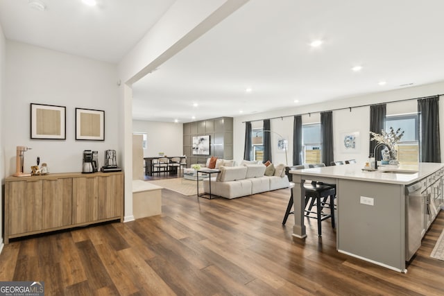 kitchen featuring dark wood-type flooring, a sink, light countertops, dishwasher, and a kitchen bar