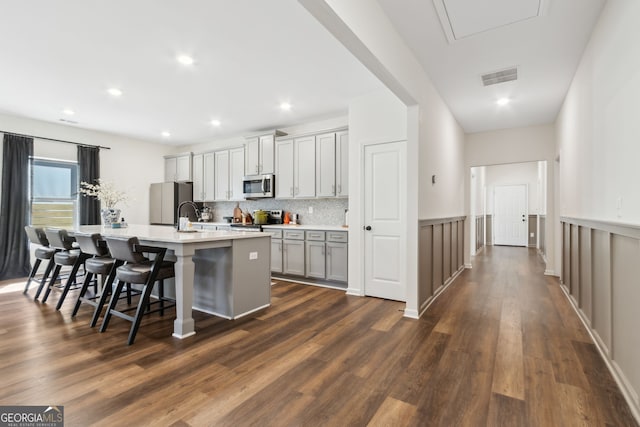 kitchen with a center island with sink, stainless steel appliances, light countertops, visible vents, and a kitchen bar