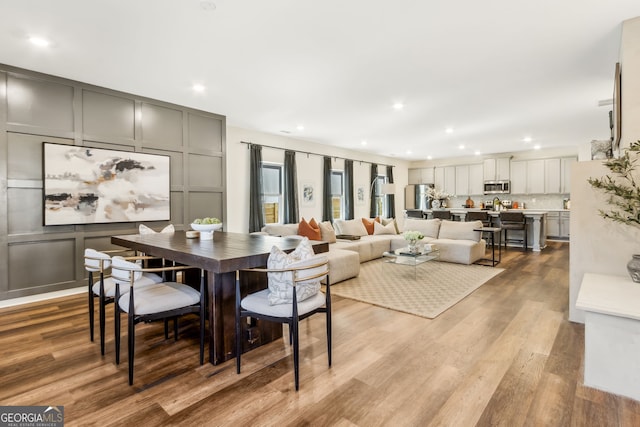 dining room with recessed lighting, a decorative wall, and wood finished floors