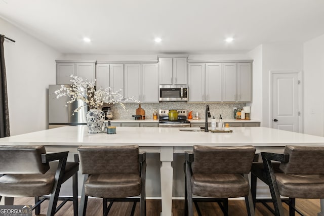 kitchen with gray cabinetry, a spacious island, light countertops, appliances with stainless steel finishes, and decorative backsplash