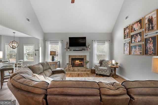 living area with a brick fireplace, wood finished floors, visible vents, and a notable chandelier