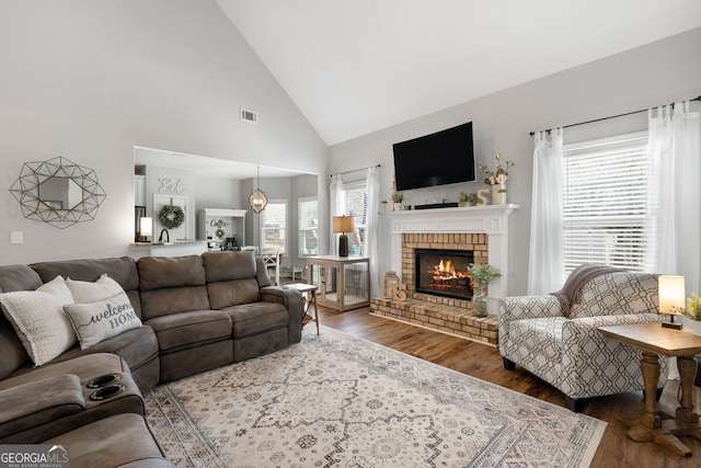 living area with a wealth of natural light, a brick fireplace, visible vents, and wood finished floors