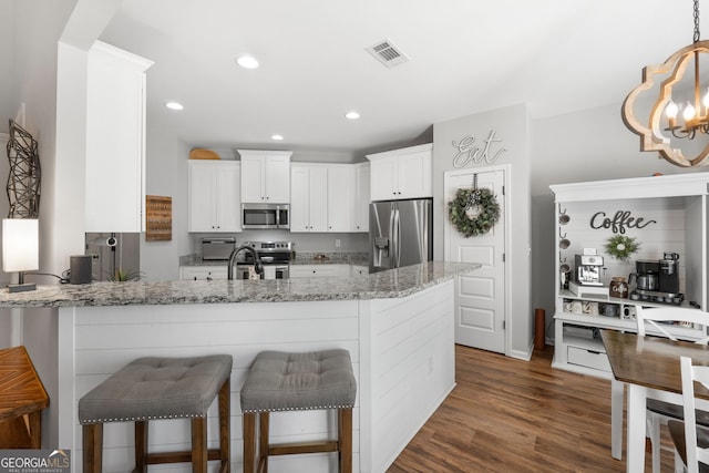 kitchen featuring light stone counters, a peninsula, dark wood-style flooring, visible vents, and appliances with stainless steel finishes