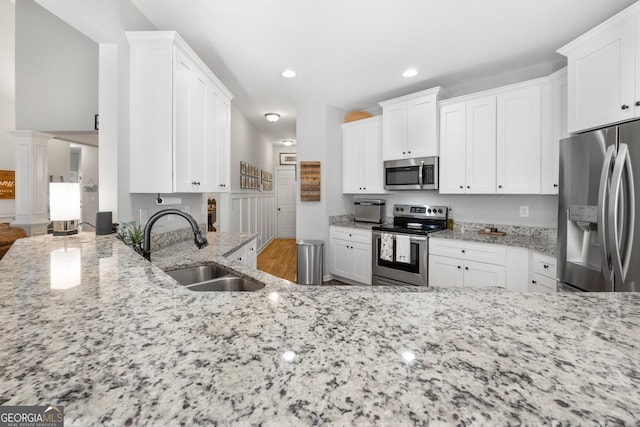 kitchen with recessed lighting, a sink, white cabinetry, appliances with stainless steel finishes, and light stone countertops