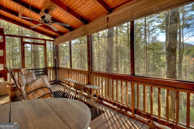 sunroom / solarium with a forest view, wooden ceiling, lofted ceiling with beams, and a ceiling fan