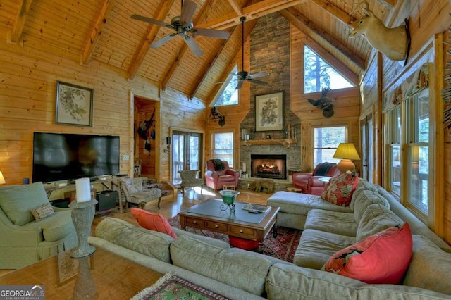 living area with vaulted ceiling with beams, a stone fireplace, wooden ceiling, and wooden walls