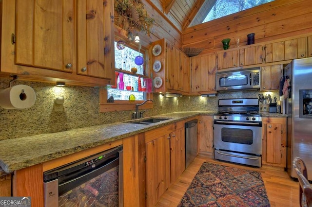 kitchen with lofted ceiling, wine cooler, appliances with stainless steel finishes, brown cabinets, and a sink