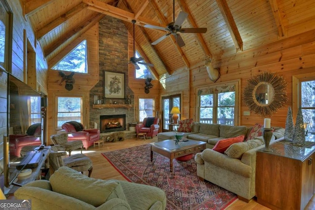 living room featuring vaulted ceiling with beams, a stone fireplace, wooden ceiling, wooden walls, and wood finished floors