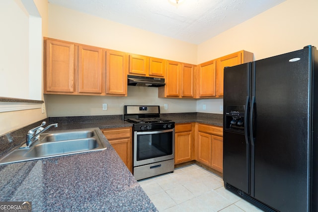 kitchen featuring light tile patterned flooring, a sink, gas range, under cabinet range hood, and black fridge