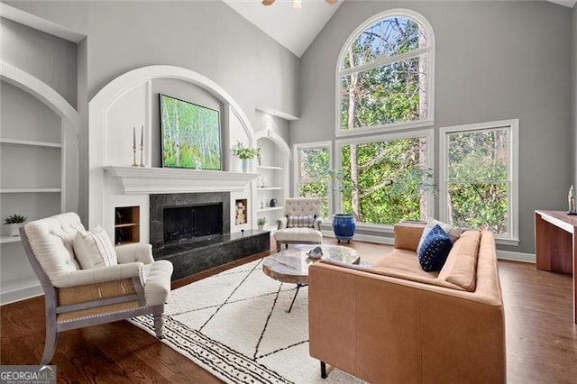 living room with built in shelves, a wealth of natural light, a fireplace, and wood finished floors