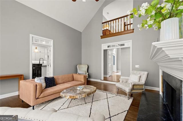 living room featuring baseboards, ceiling fan, a fireplace with flush hearth, wood finished floors, and high vaulted ceiling