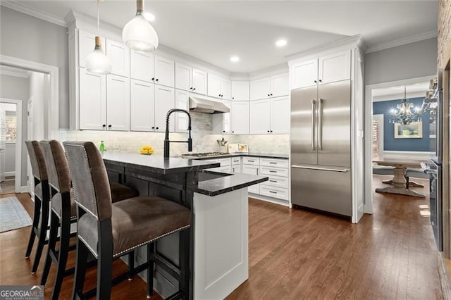 kitchen featuring a peninsula, stainless steel built in fridge, under cabinet range hood, and white cabinets