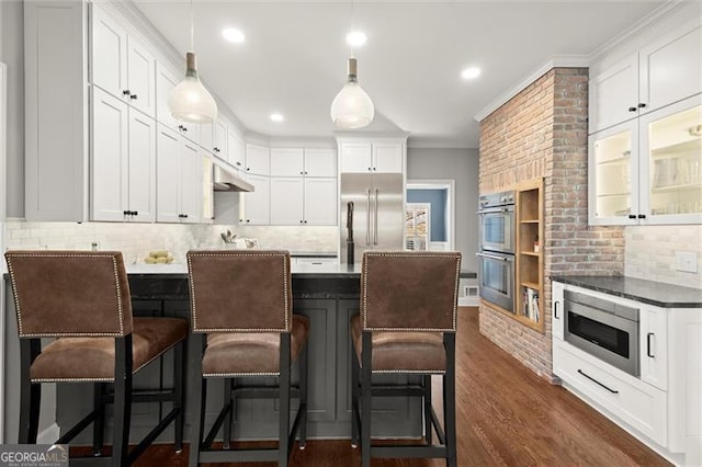 kitchen featuring white cabinets, under cabinet range hood, a peninsula, and built in appliances