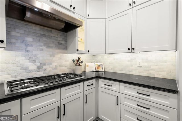 kitchen featuring under cabinet range hood, stainless steel gas cooktop, white cabinets, and backsplash