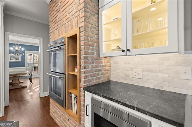 kitchen featuring dark wood finished floors, crown molding, stainless steel appliances, dark countertops, and glass insert cabinets