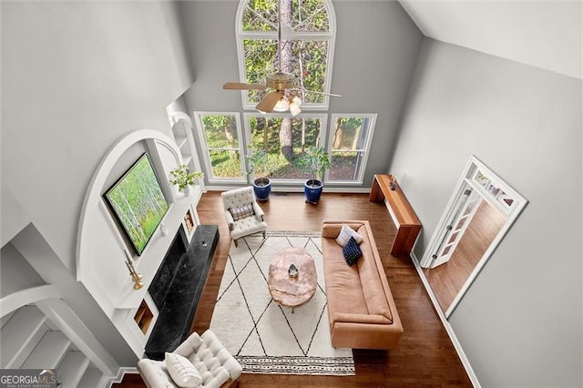 living area with ceiling fan, high vaulted ceiling, wood finished floors, and baseboards